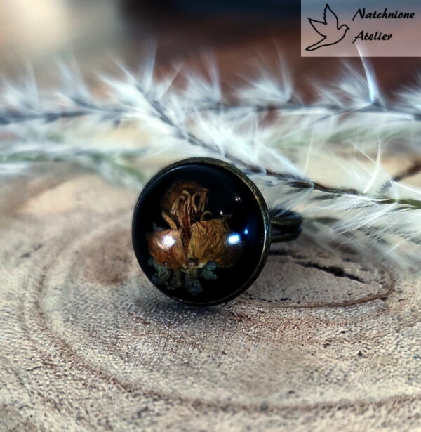 Ręcznie robiony pierścionek z kwiatem rzepaku zatopionym w żywicy na czarnym tle, styl vintage