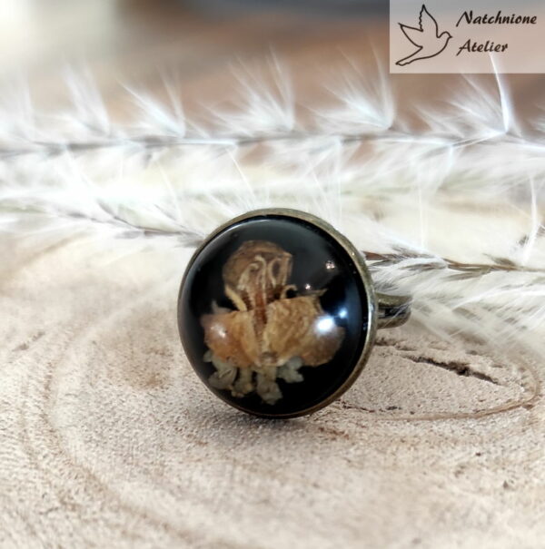 Ręcznie robiony pierścionek z kwiatem rzepaku zatopionym w żywicy na czarnym tle, styl vintage